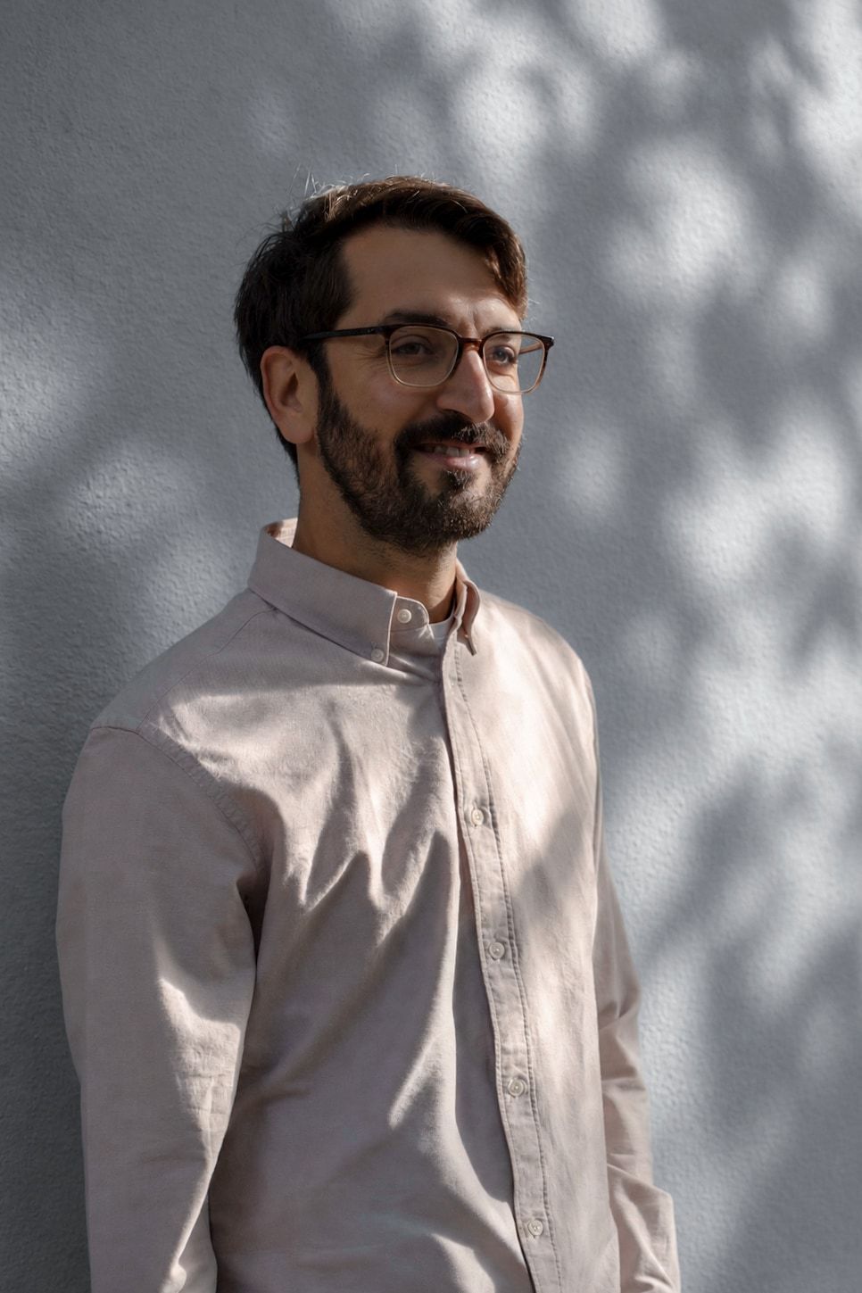 Namir in a pale shirt, smiling and looking to the side, in front of a sunlit textured wall