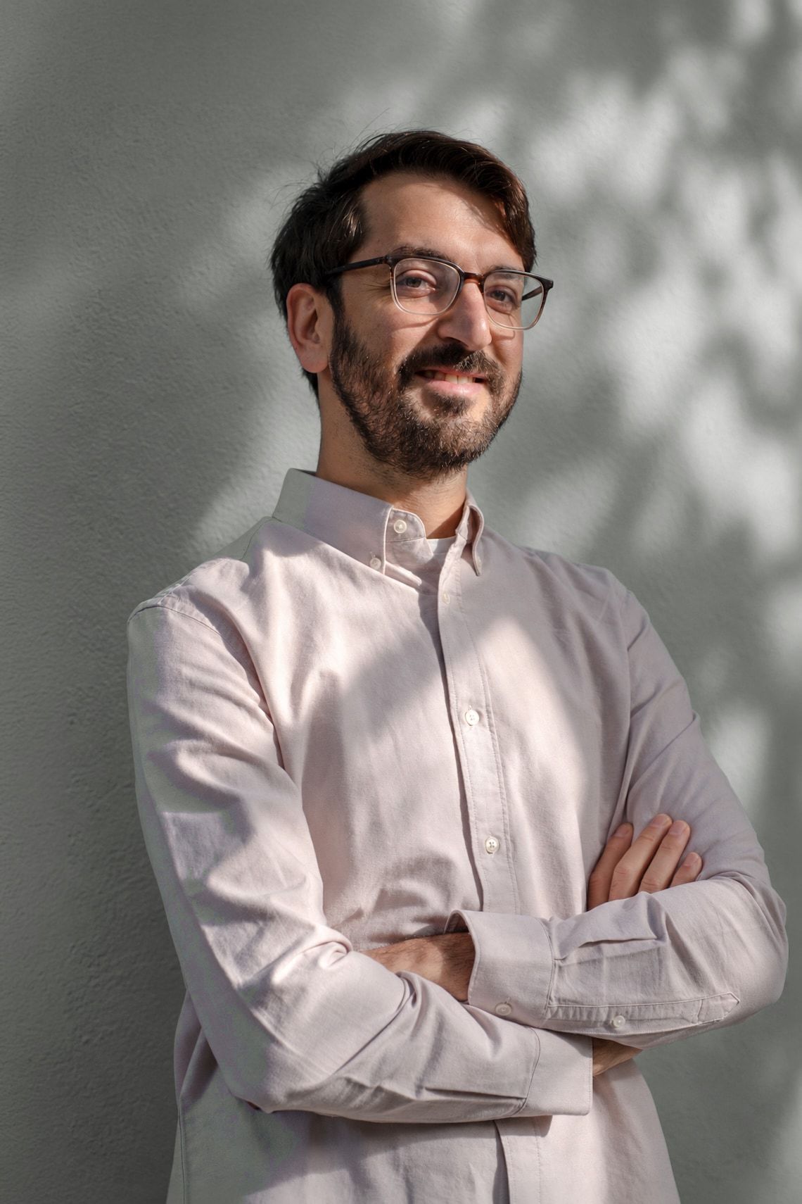 Namir Sayed-Ahmad Baraza, arms crossed and smiling at the camera, in front of a sunlit textured wall